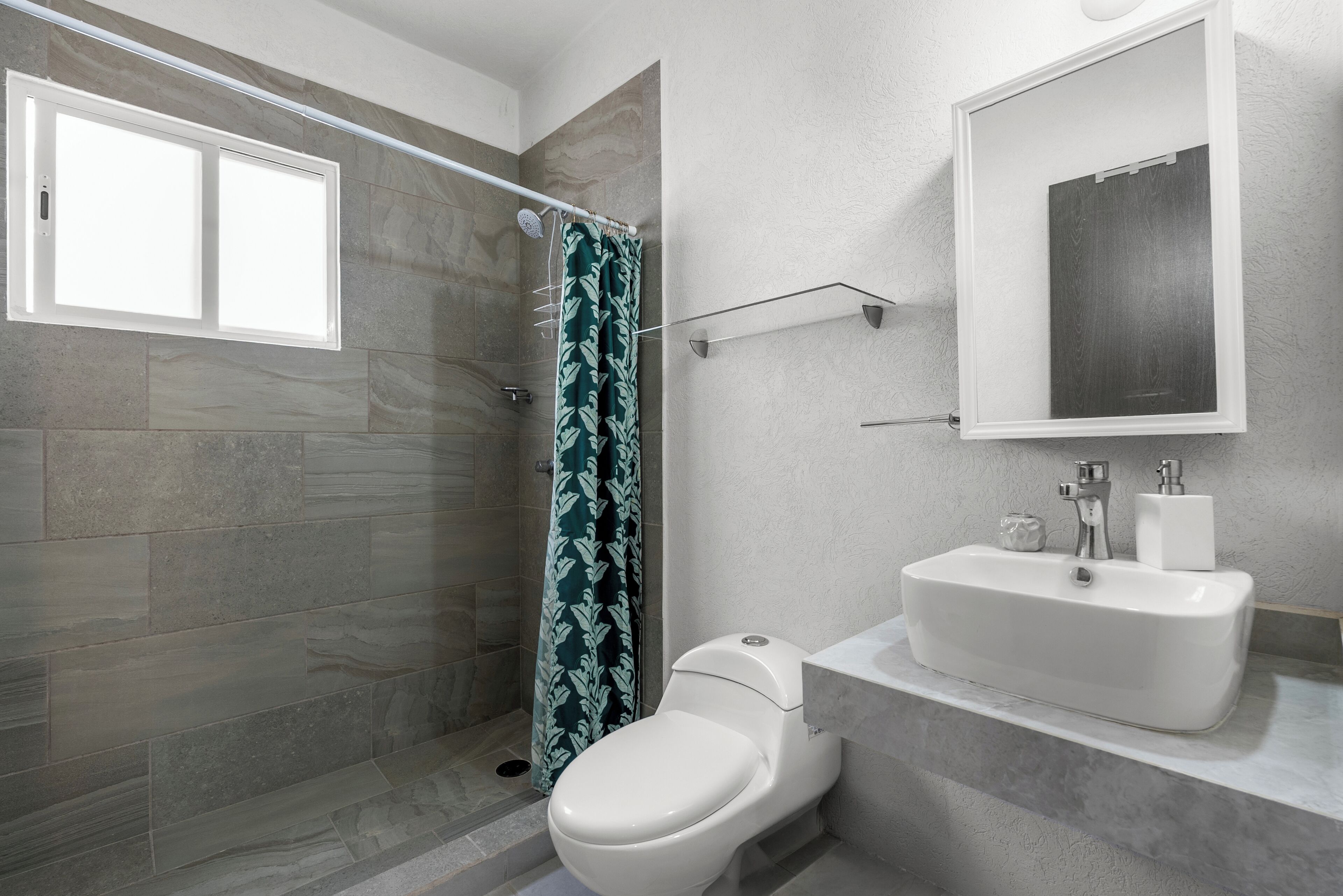 A bathroom with a shower, toilet, sink, and a mirror.