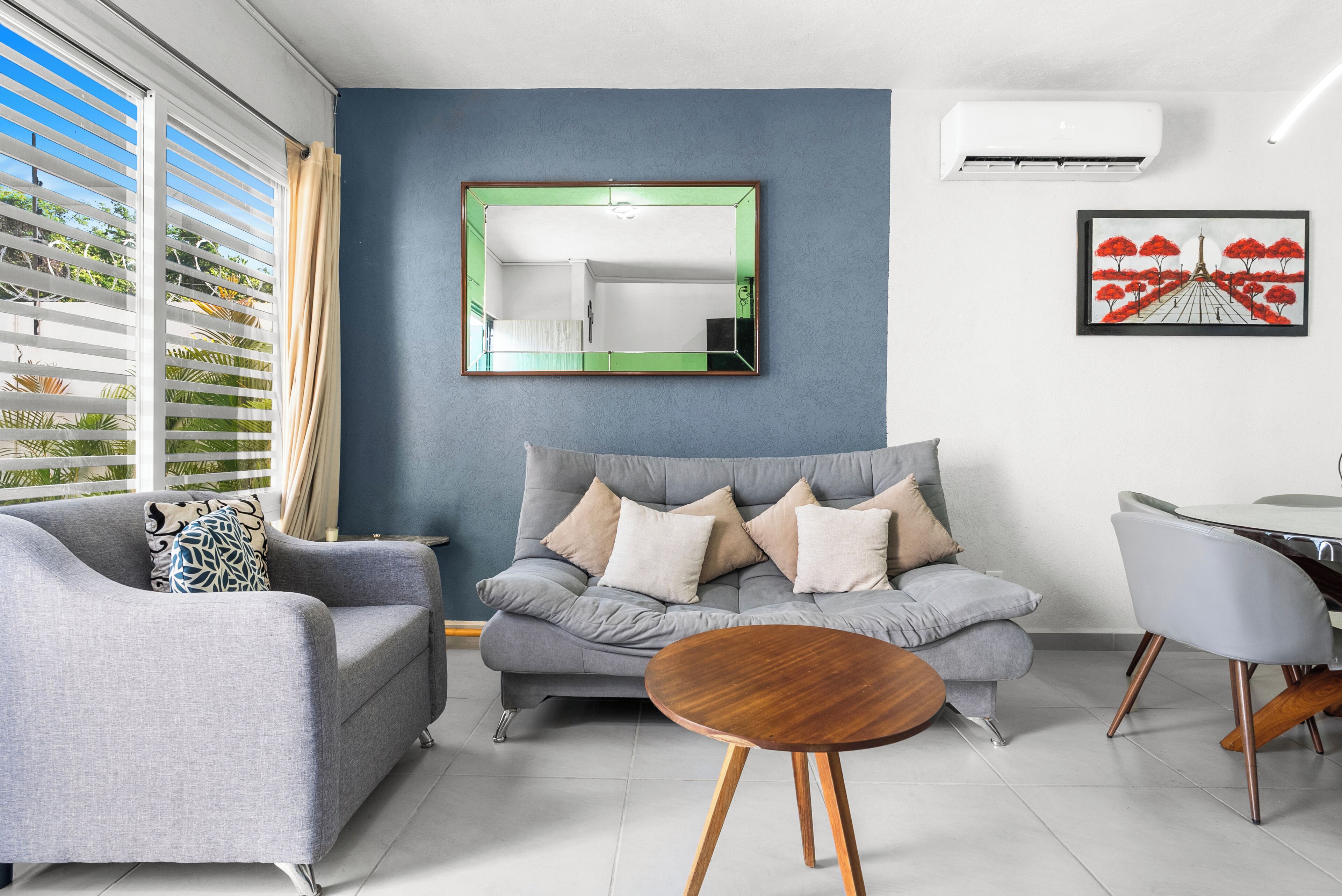 Una sala moderna con un sofá gris, una mesa de centro redonda de madera y un espejo grande en la pared.