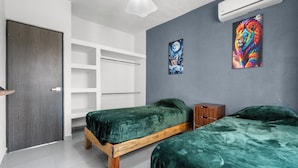 A bedroom with two wooden beds, a white wardrobe, a small wooden nightstand, and a colorful abstract painting on the wall.
