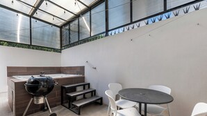 A patio with a barbecue grill, a hot tub, and a seating area with chairs and a table.