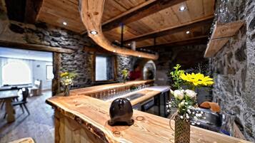 A rustic interior with a wooden bar, stone walls, and a stone fireplace.