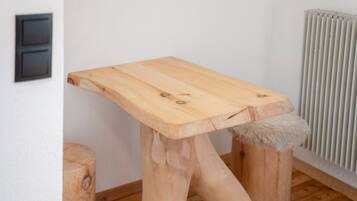 Eine Katzenkralle aus Holz mit flacher Ablage und einem fellartigen Fußhocker, platziert vor einer Wand mit Heizkörper und Stromverteiler.