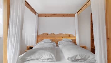 A bedroom with a wooden headboard, two white beds with pillows, and sheer white curtains.