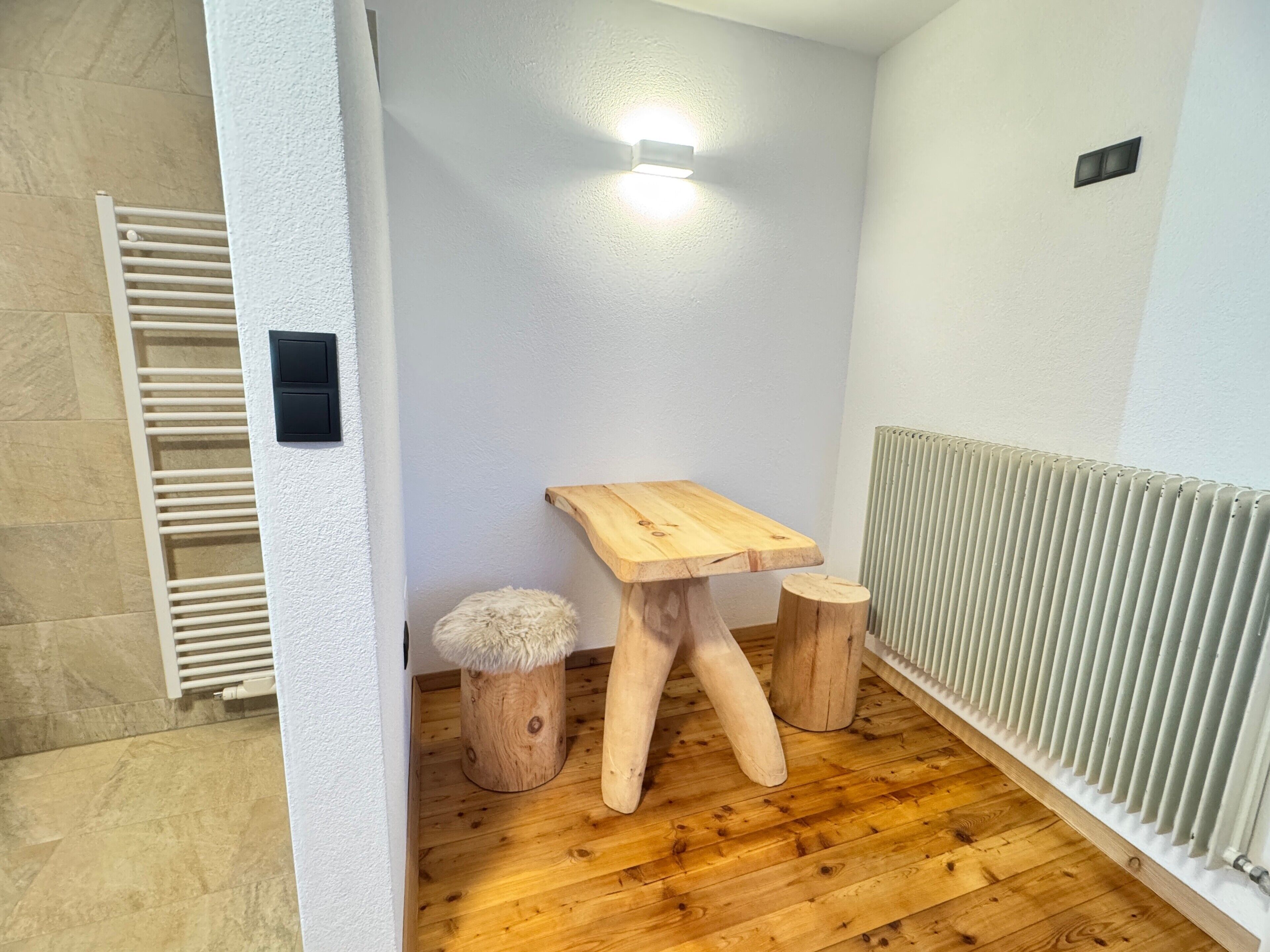 A small bathroom with a wooden stool, a radiator, and a towel rack.