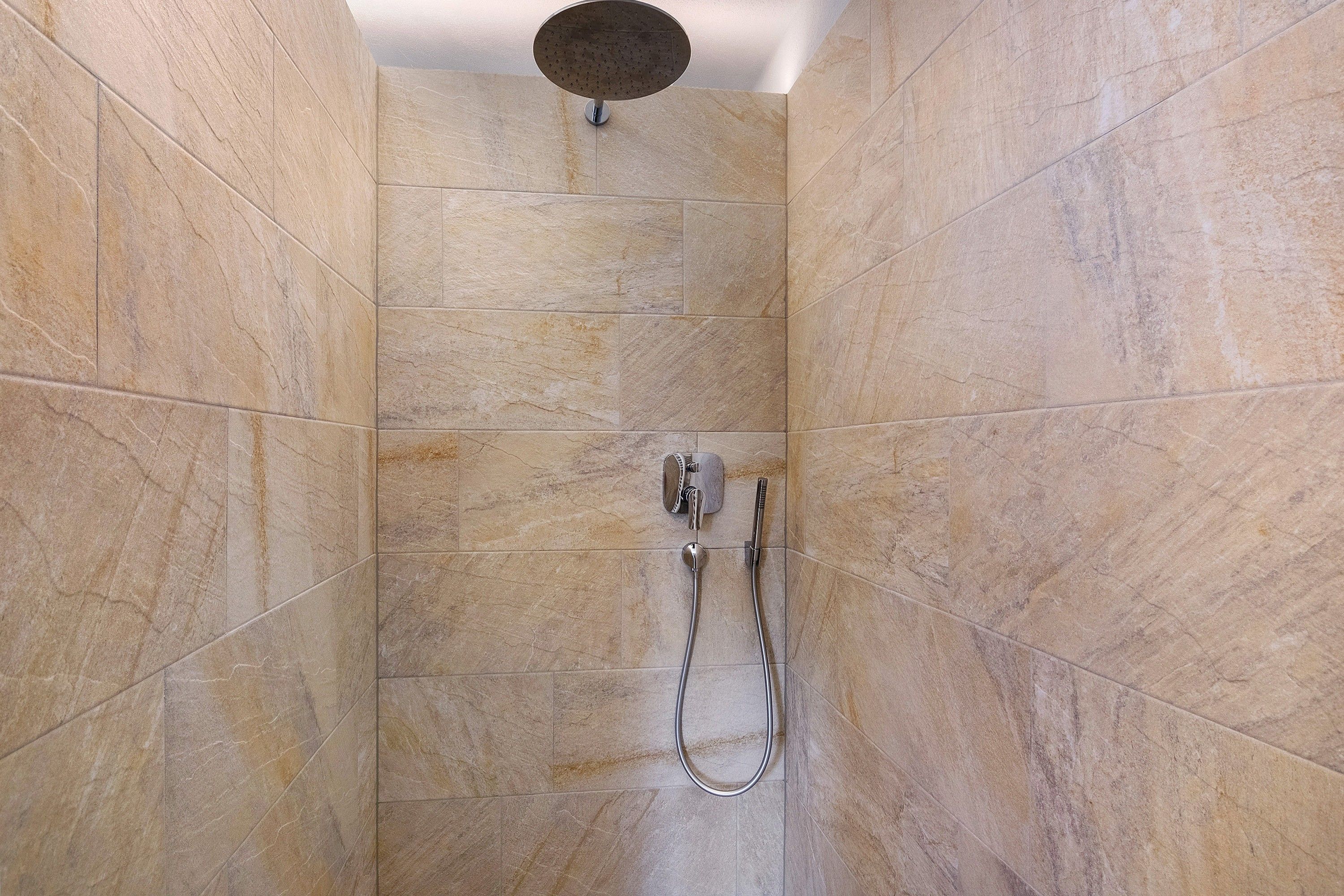 Une douche équipée d’un pommeau de douche à main et d’un robinet fixé au mur.
