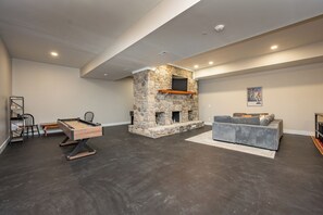 A modern living room with a stone fireplace, a pool table, and a grey sofa. - Stylish Lakefront Deep Creek Retreat w/ Hot Tub (Swanton)