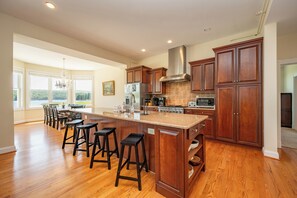 A spacious kitchen with a large island, wooden cabinets, and a view to the outdoors. - Stylish Lakefront Deep Creek Retreat w/ Hot Tub (Swanton)
