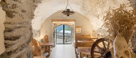 A rustic interior with stone walls, wooden furniture, and a view through an arched doorway.