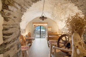 Interior rústic amb parets de pedra, mobles de fusta i una vista a través d'una porta d'arc.