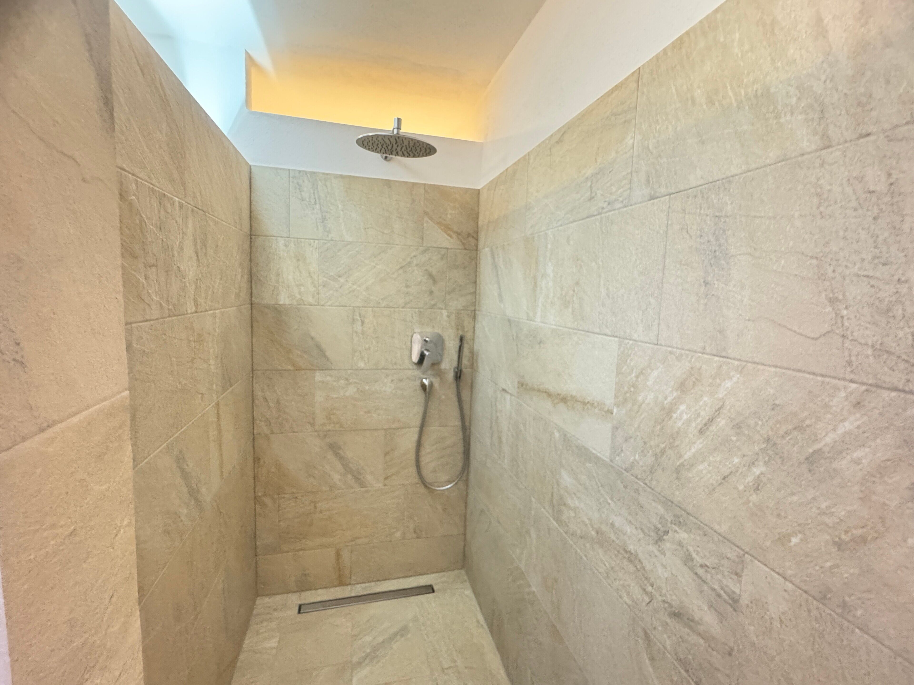 Une douche équipée d’un pommeau de douche à main et d’un robinet fixé au mur.