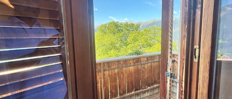 Un balcon en bois offrant une vue sur des arbres verdoyants et des montagnes.