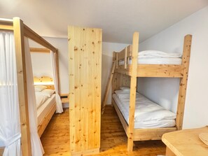 Quarto com beliches, divisória de madeira e uma pequena mesa.