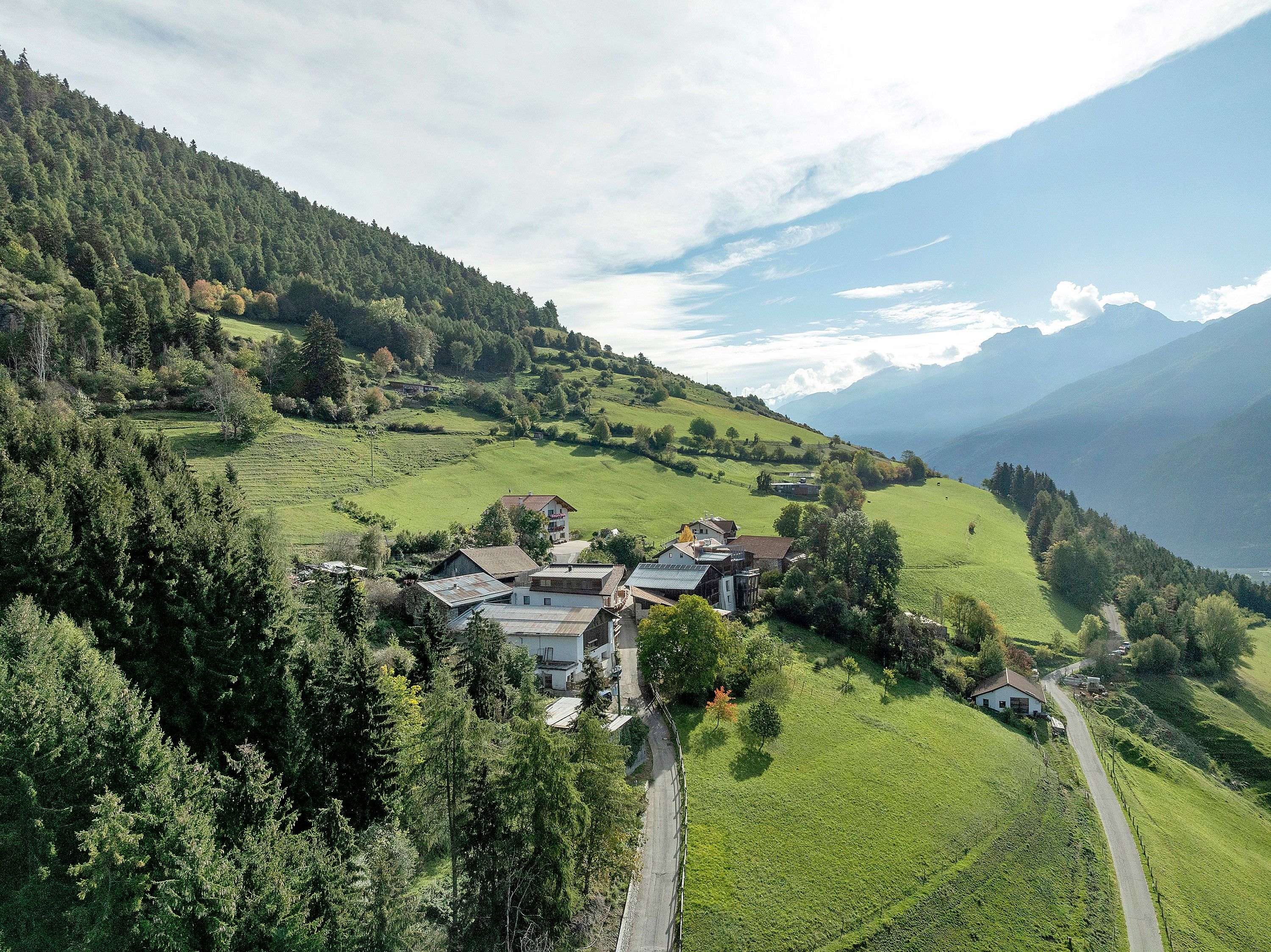 Un paisaje rural con un grupo de casas rodeado de vegetación exuberante y montañas al fondo.