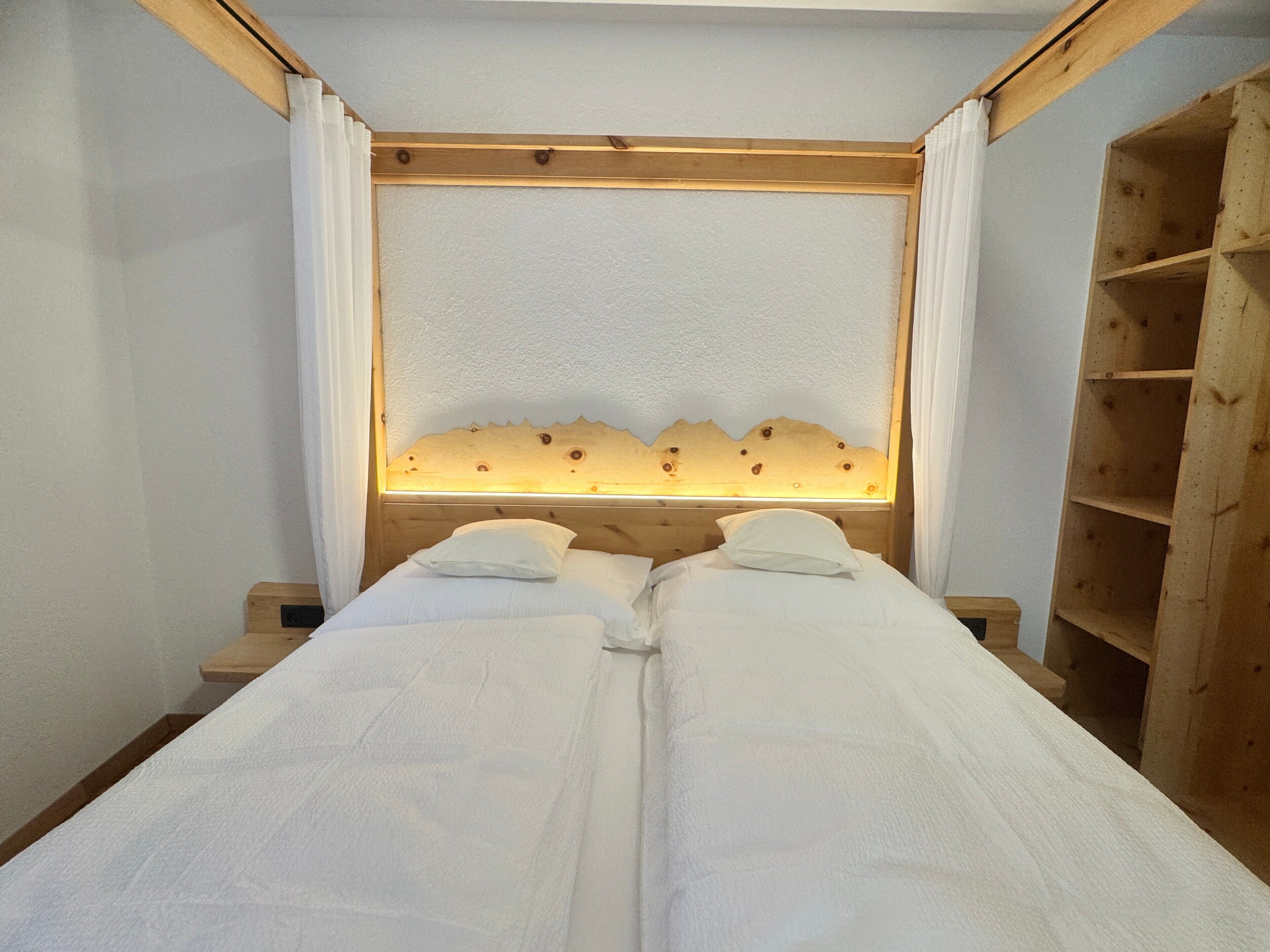Ein Zimmer mit zwei Betten, einem Holzkopfstück und einer beleuchteten Tafel sowie einer Holzregaleinheit.