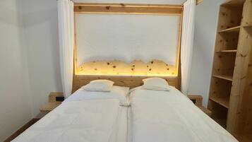 Ein Zimmer mit zwei Betten, einem Holzkopfstück und einer beleuchteten Tafel sowie einer Holzregaleinheit.
