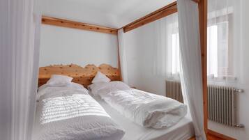A double bed with a wooden headboard, white bedding, and sheer curtains.