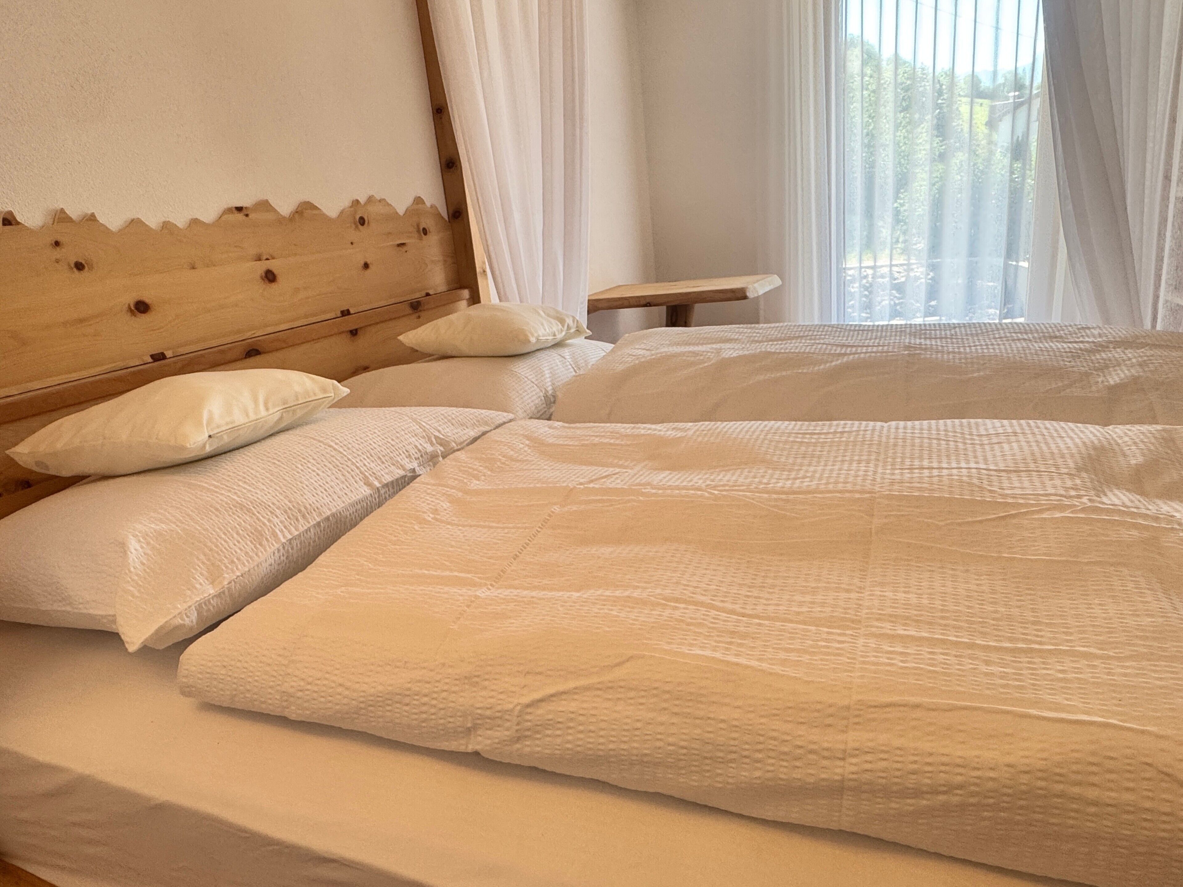 A bedroom with two beds, a wooden headboard, and a window with sheer curtains.