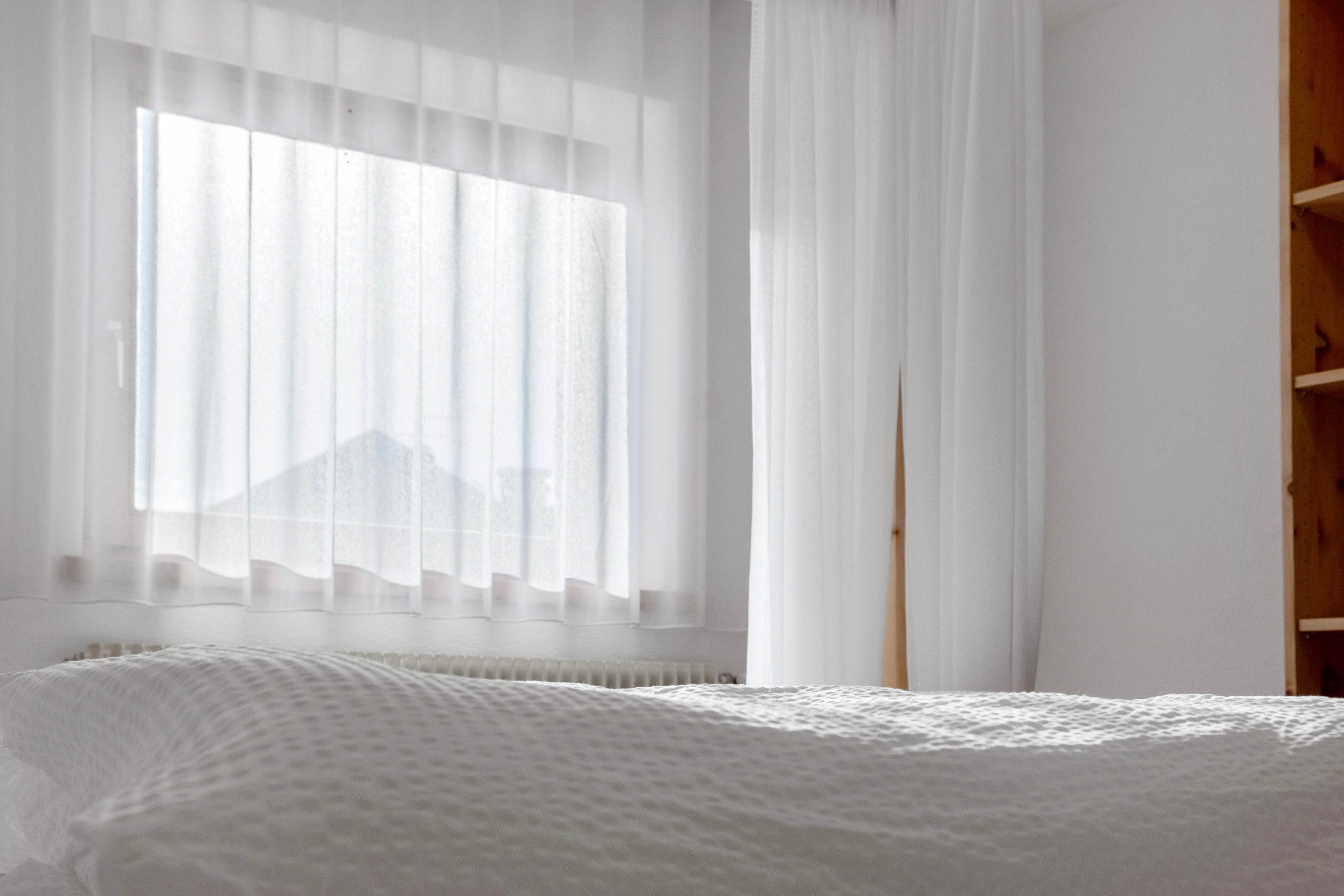 Une chambre avec un lit, une fenêtre avec des rideaux légers et une armoire en bois.