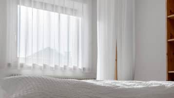 Une chambre avec un lit, une fenêtre avec des rideaux légers et une armoire en bois.