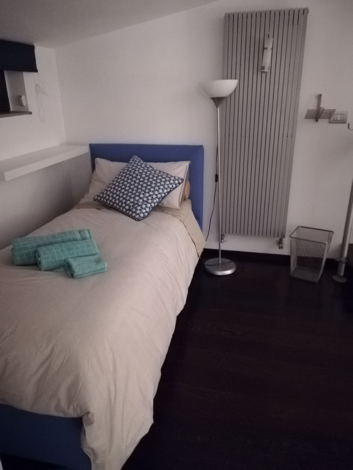 A neatly made bed with a blue headboard, a bedside lamp, and a window with blinds.