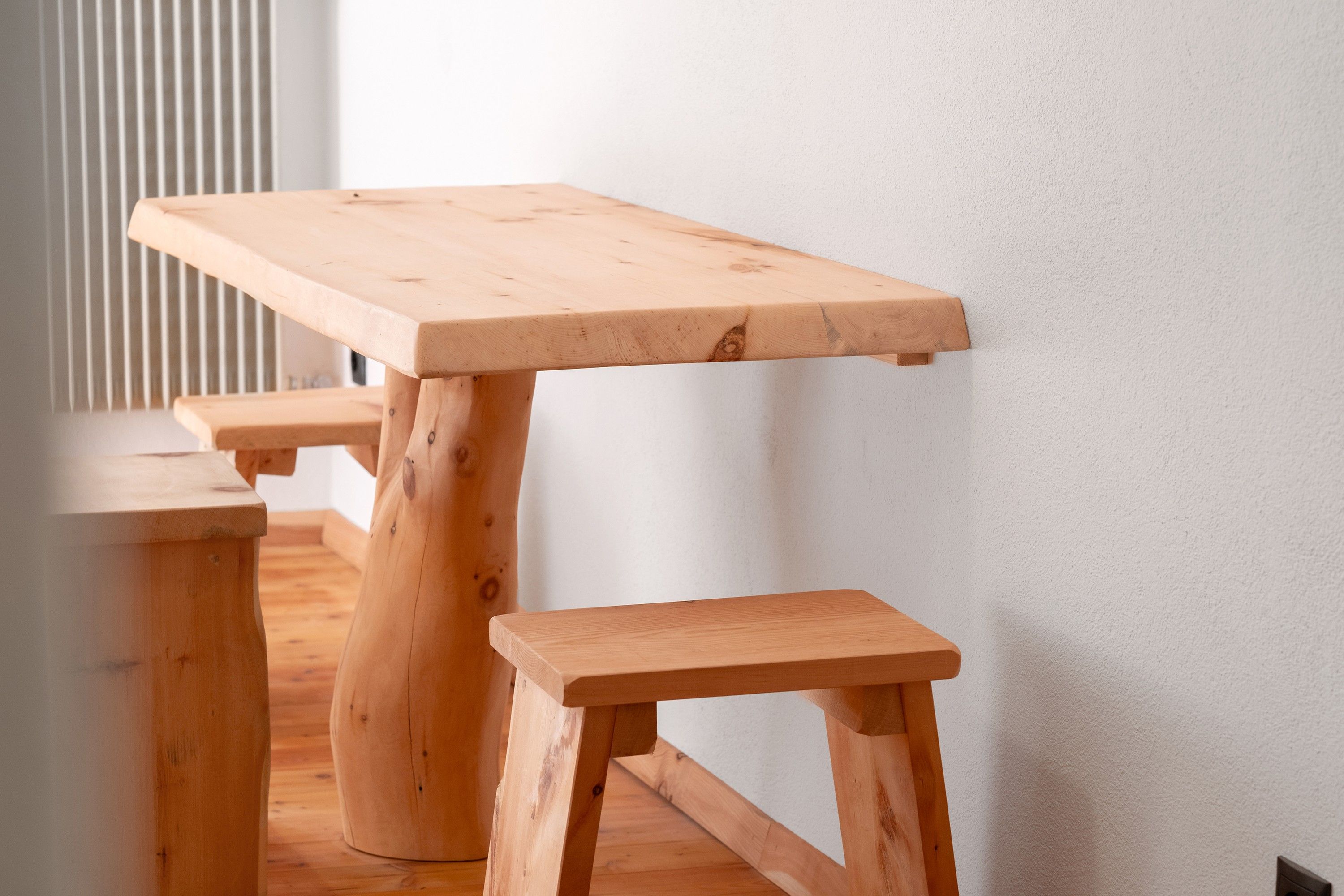 A wooden table with a bench, positioned against a white wall.