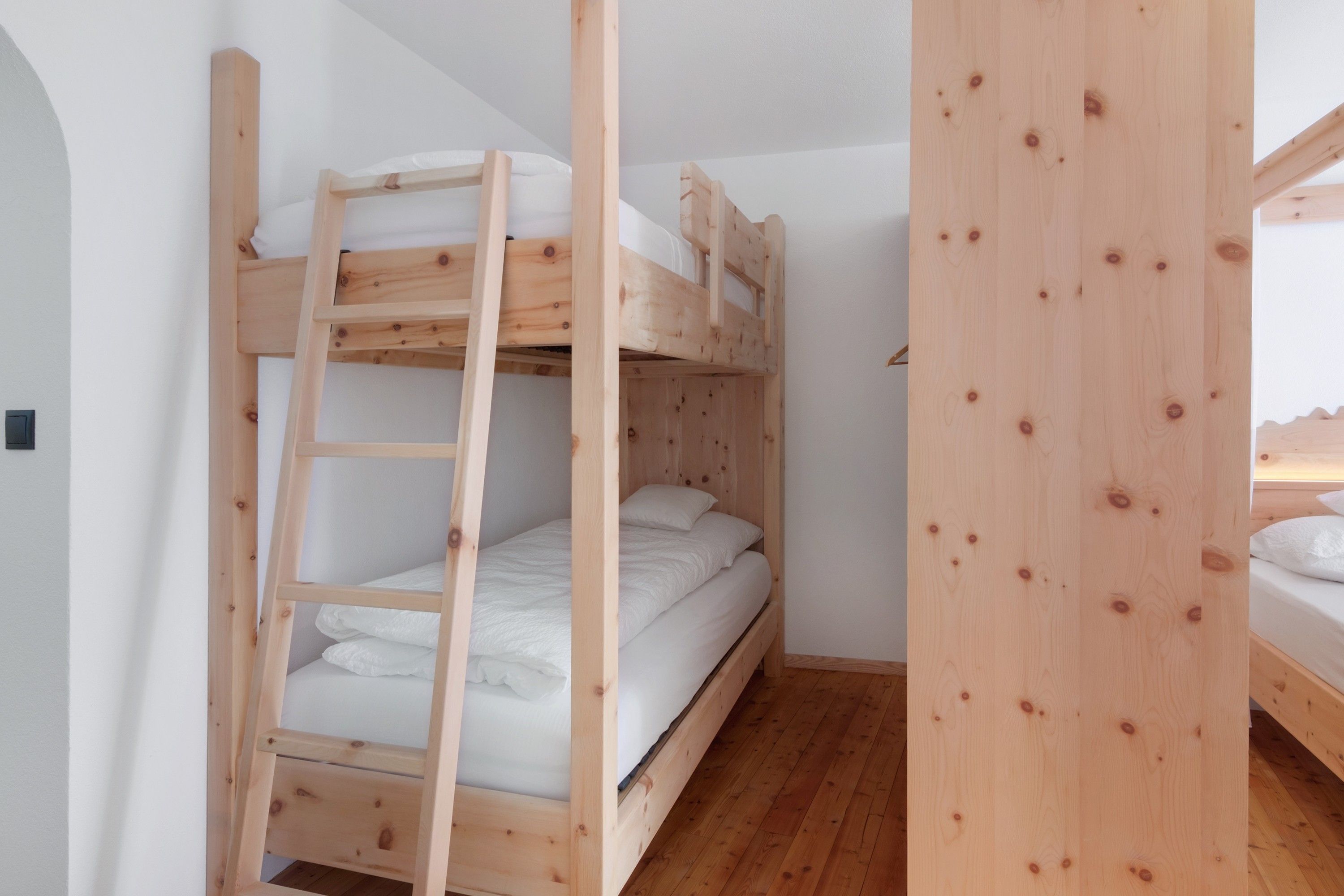 Habitació amb lliteres de fusta i roba de llit blanca.