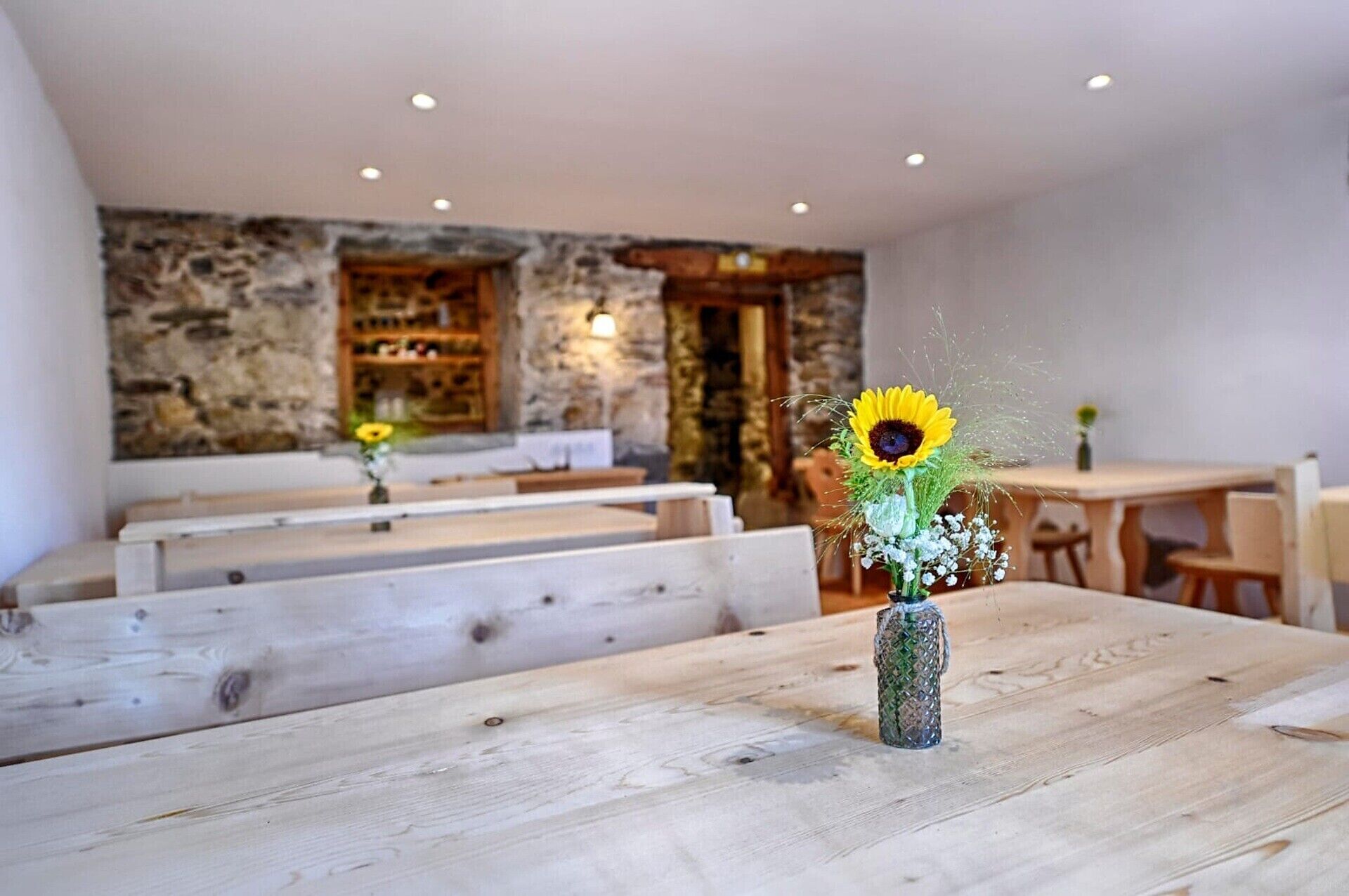 A restaurant with wooden tables and benches, a stone wall, and a vase with a sunflower.