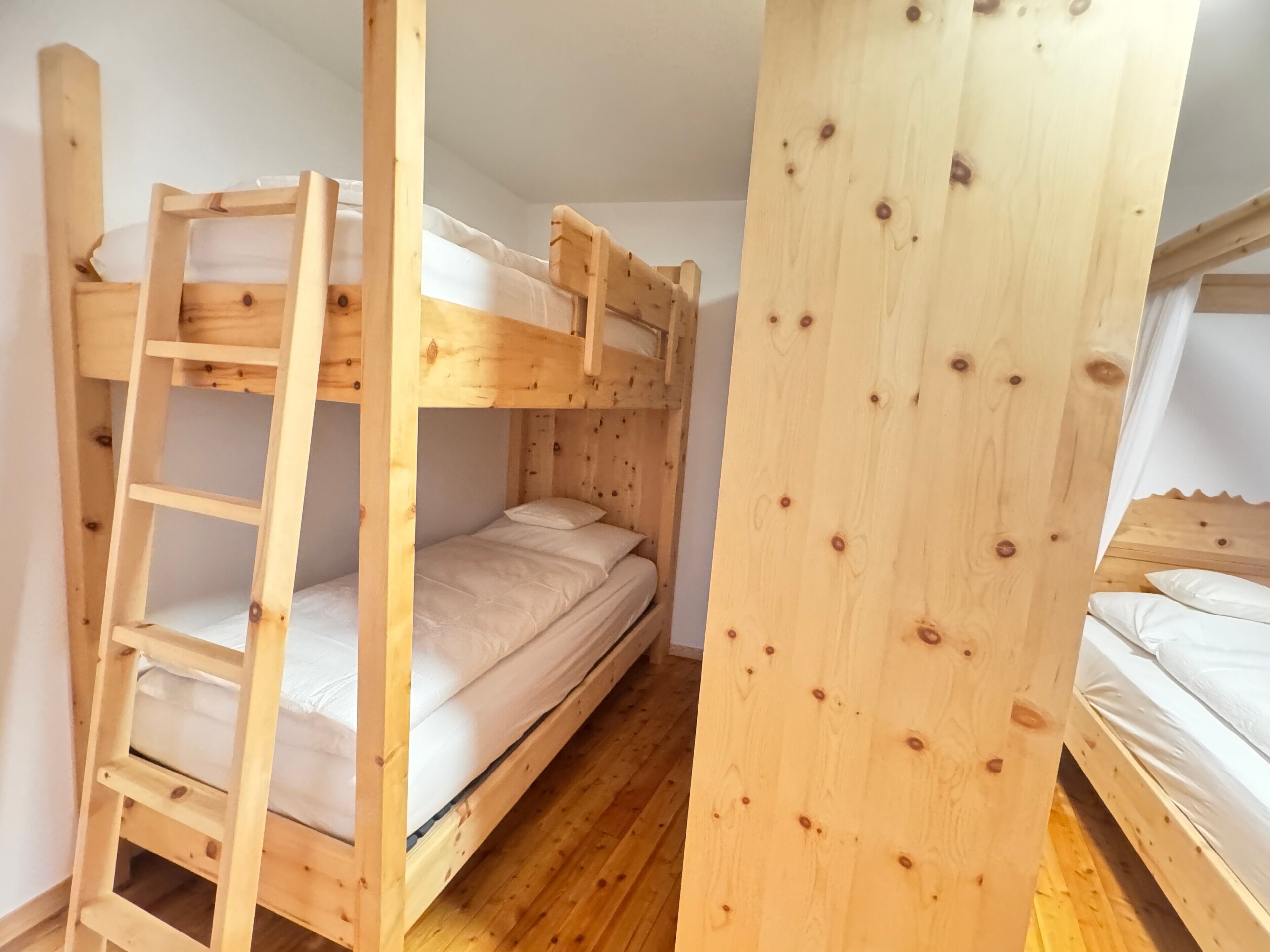 A bunk bed room with a wooden ladder and a bunk bed with a mattress and pillow.