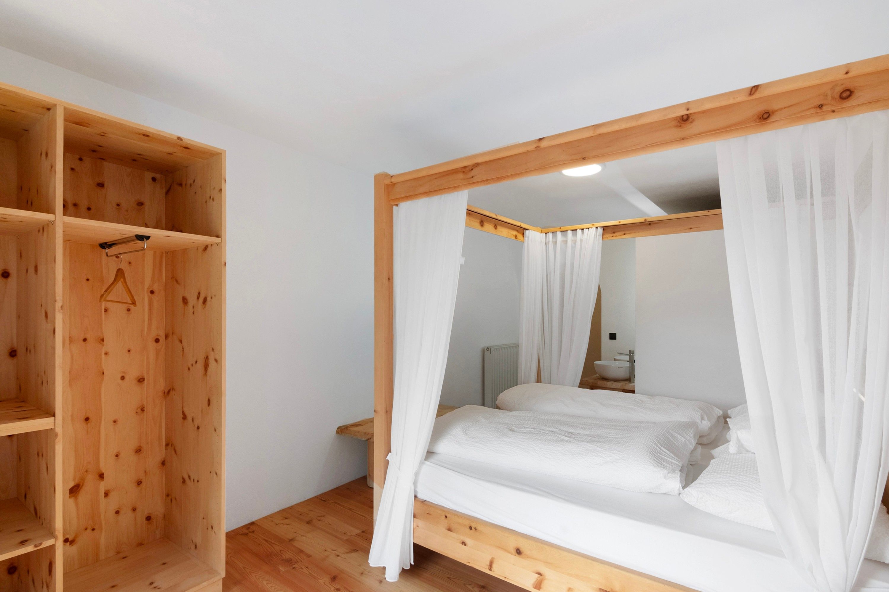 Una camera da letto con un letto a baldacchino in legno, biancheria da letto bianca e un armadio in legno con una barra appendiabiti.