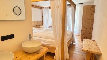 Ein Schlafzimmer mit Himmelbett, Nachttisch aus Holz, weißem Waschbecken und einer Holzbank.