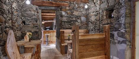 A rustic interior with stone walls, wooden benches, and a central table.