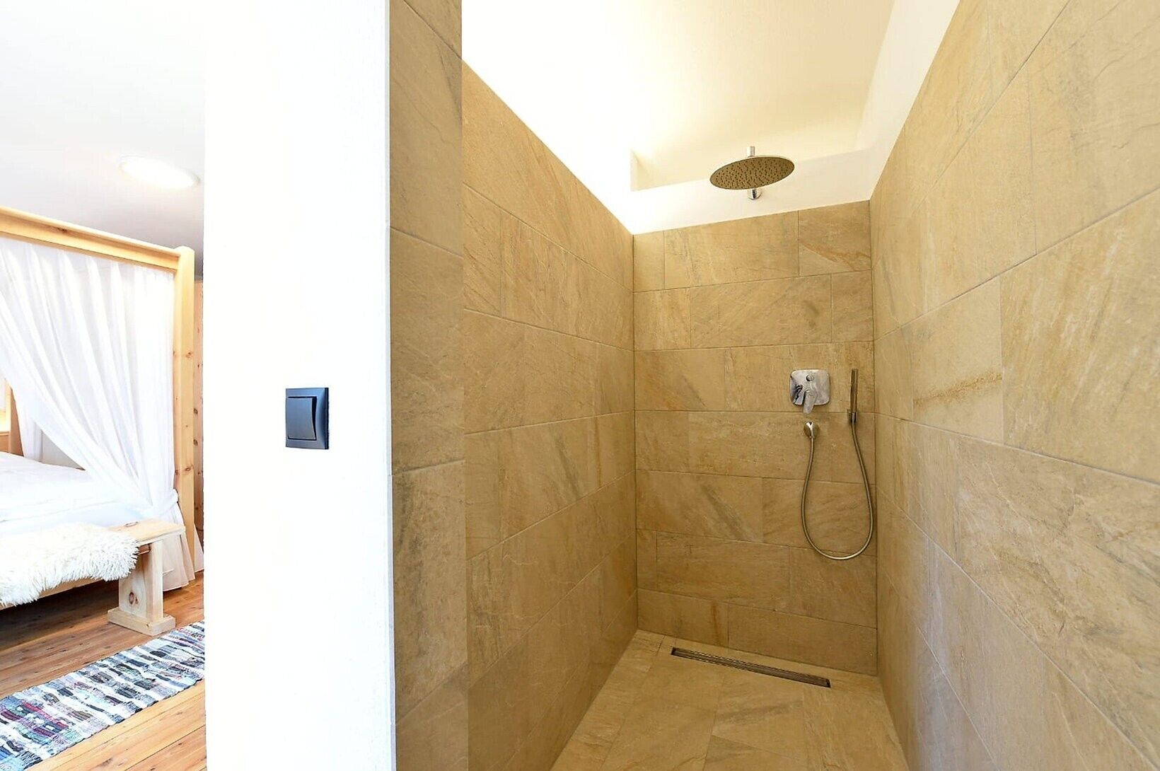 A bedroom with a bed and a shower area with tiled walls and a showerhead.