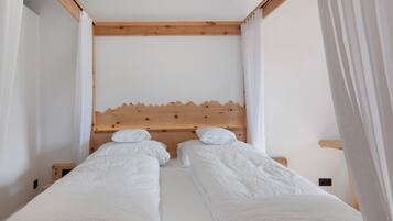 A room with two single beds, wooden headboards, white bedding, and sheer curtains.