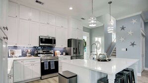 A modern kitchen with white cabinetry, stainless steel appliances, and a central island with stools. - Ultimate Waterfront Escape | Pool, Dock, & Views (Jamaica Beach)
