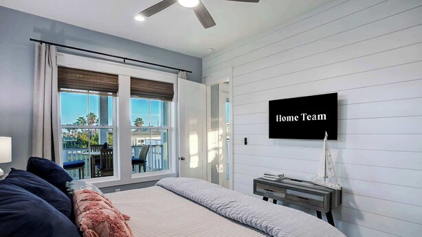 A bedroom with a large bed, a TV mounted on the wall, and a view of the outdoors through the window. - Ultimate Waterfront Escape | Pool, Dock, & Views (Jamaica Beach)