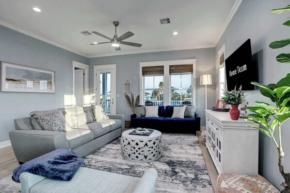 Ein Wohnzimmer mit grauem Sofa, blauem Sofa, Couchtisch und Deckenventilator.