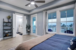 Quarto com cama, janela com vista, ventoinha no teto e porta de acesso a um banheiro.
