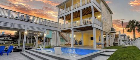 A two-story house with a pool, outdoor seating, and a covered patio area.