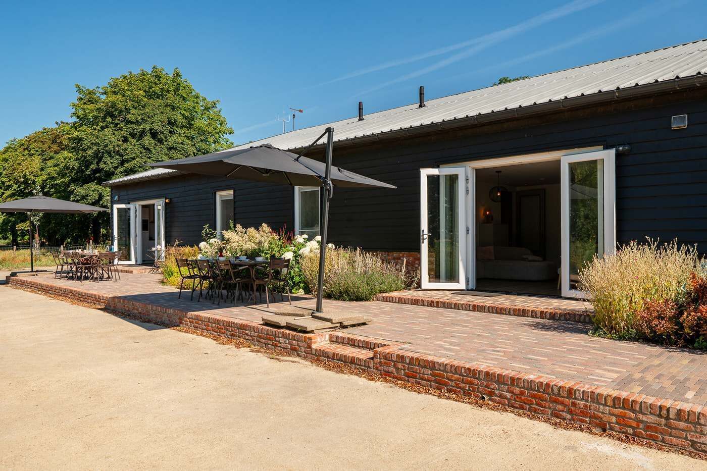 Un bâtiment doté d’un patio comprenant une table et des chaises, un espace salon couvert et un chemin en briques menant à l’entrée.