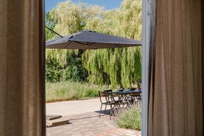 An outdoor patio with a table and chairs, a large umbrella, and a weeping willow tree in the background. - Holiday home with 5 bedrooms in Ossenisse | Het Hoogland B (Ossenisse)