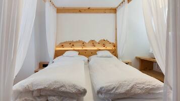 A double bed with a wooden headboard, white bedding, and sheer curtains.