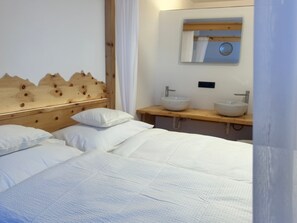 A hotel room with a wooden headboard, two white sinks, and a bed with white linens. - Room '6 Doppelzimmer' with Mountain View and Wi-Fi (Casinara)