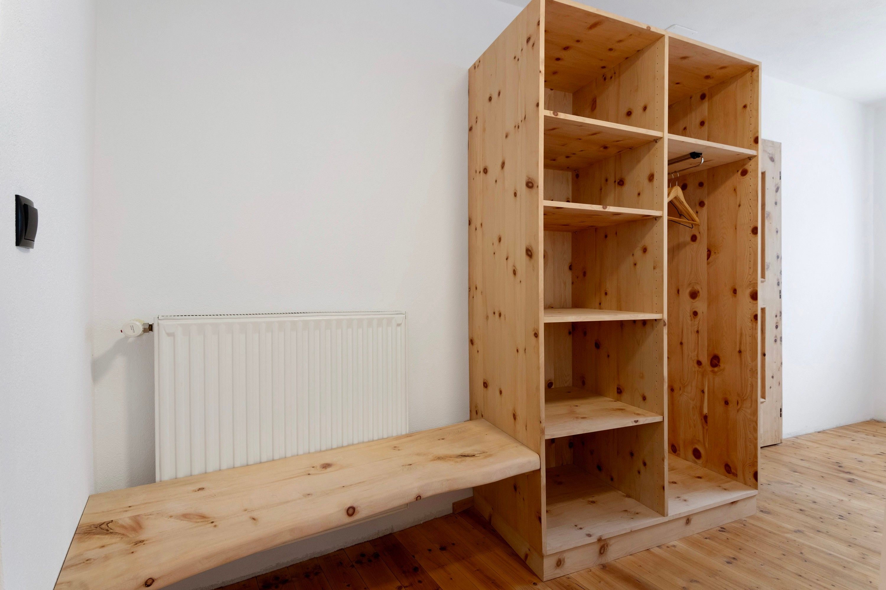A room with a wooden wardrobe, a white radiator, and a wooden bench.
