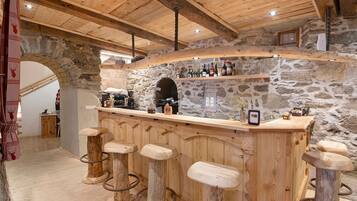 Un coin bar rustique avec des tabourets en bois, un mur en pierre en arrière-plan et une variété de bouteilles.