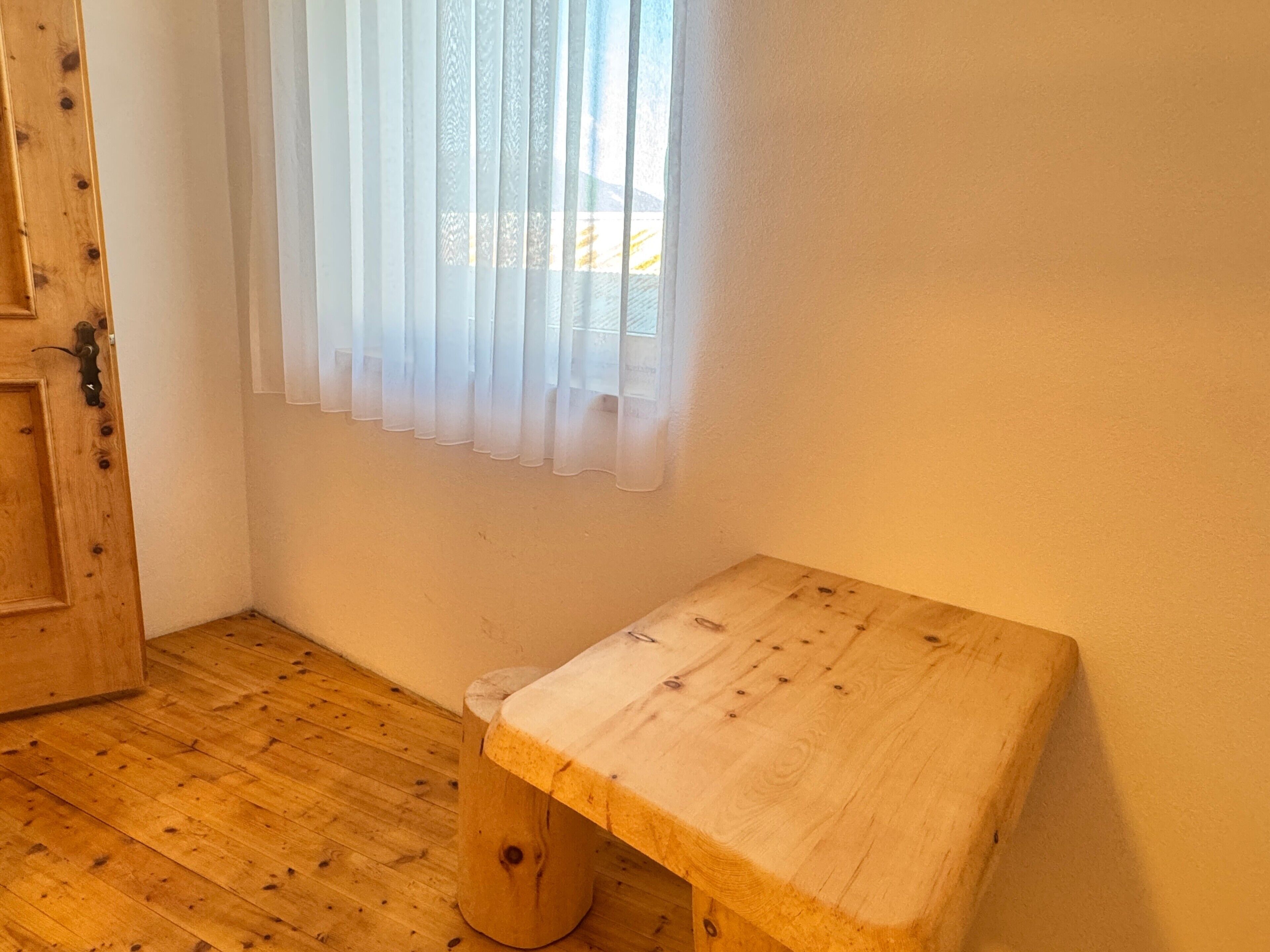 A room with a wooden bench, a door, and a window with sheer curtains.