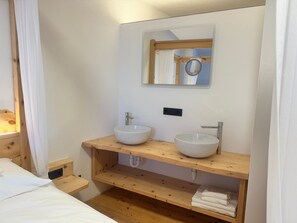 A bathroom with two sinks, a mirror, and wooden shelves. - Room '6 Doppelzimmer' with Mountain View and Wi-Fi (Casinara)