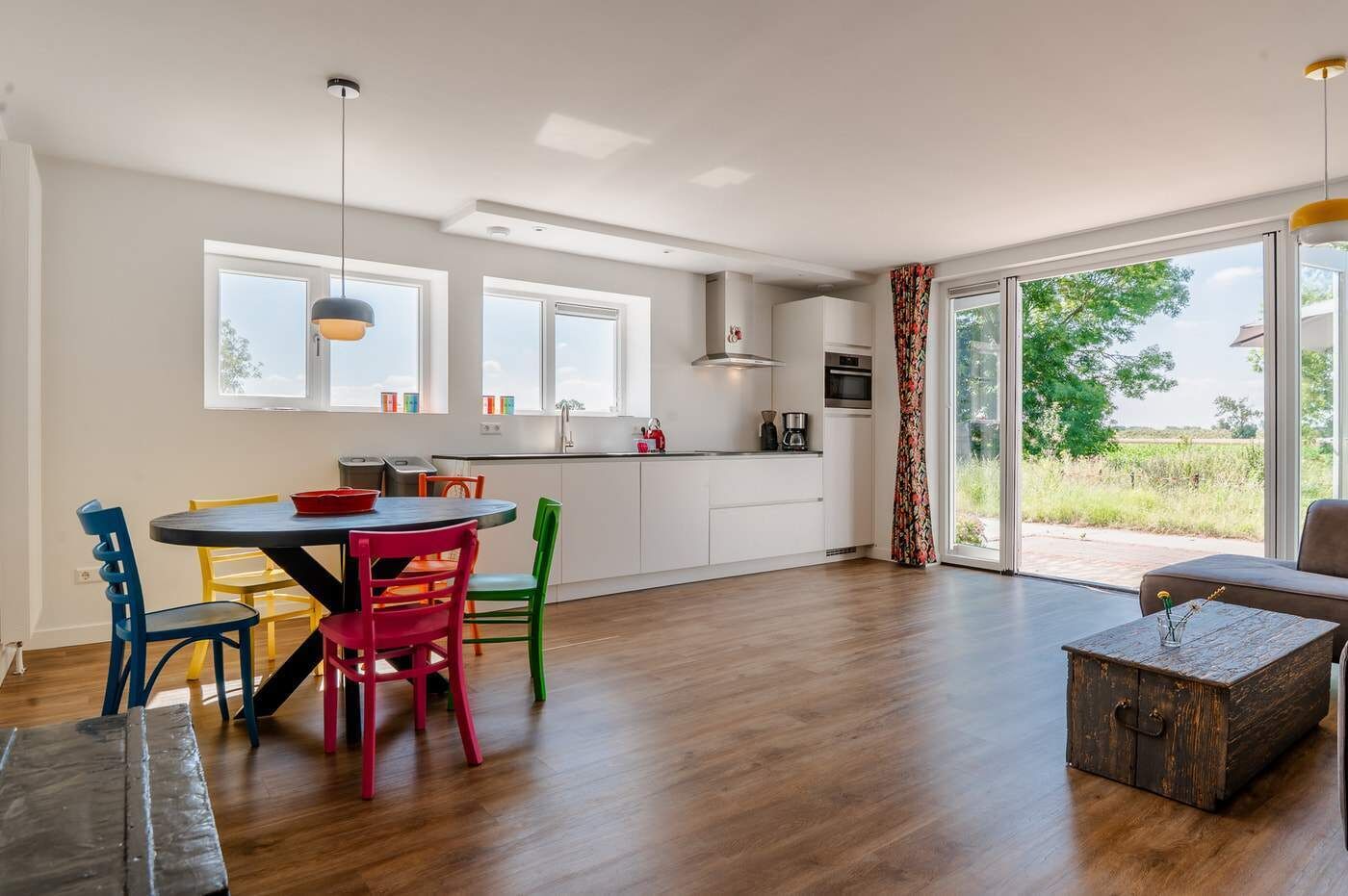 A modern kitchen with a dining area, large windows, and a view of the outdoors.