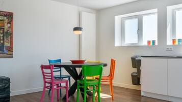 A dining area with a table and colorful chairs, a pendant light, and a kitchen area with cabinets and a window.
