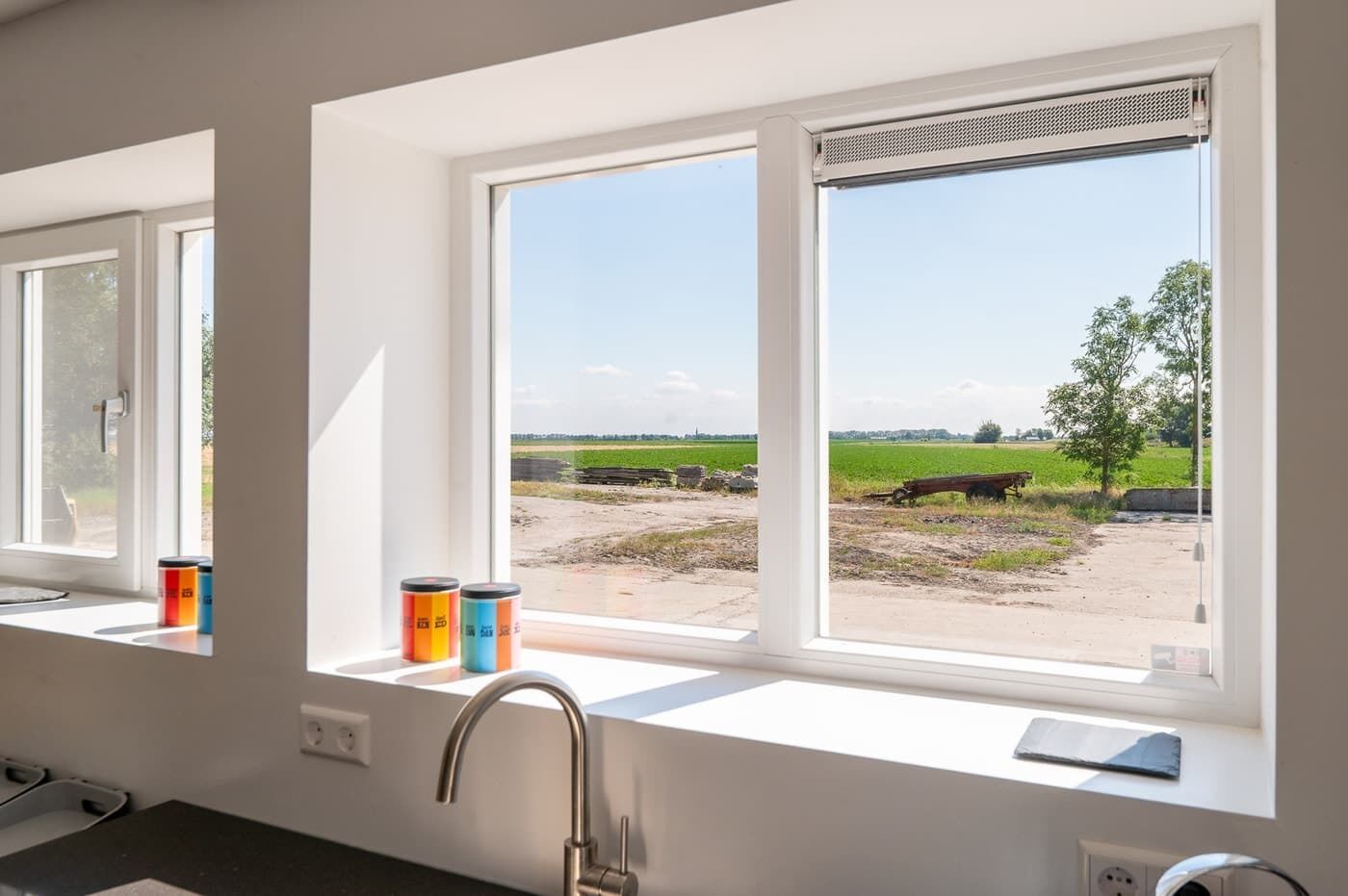 A kitchen with a window view of a rural landscape, a sink, and two containers on the windowsill.