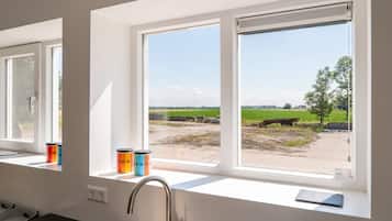 A kitchen with a window view of a rural landscape, a sink, and two containers on the windowsill.